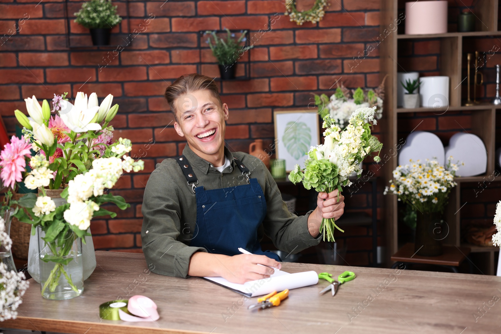 Photo of Professional florist with bouquet of flowers working at wooden table in shop