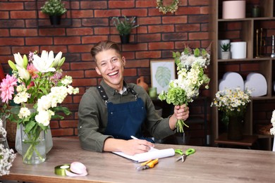 Photo of Professional florist with bouquet of flowers working at wooden table in shop