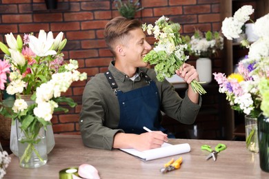 Photo of Professional florist with bouquet of flowers working at wooden table in shop
