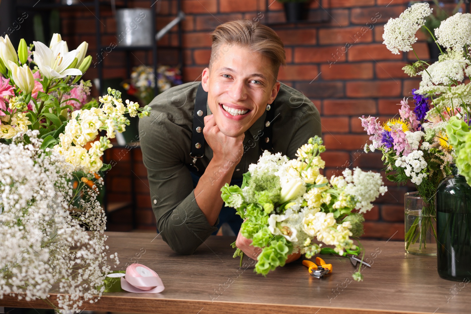 Photo of Professional florist with bouquet of flowers at wooden table in shop