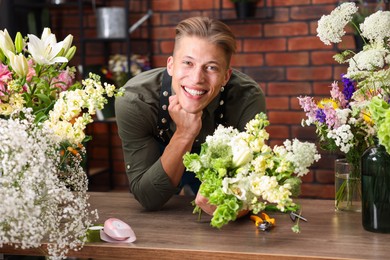 Photo of Professional florist with bouquet of flowers at wooden table in shop
