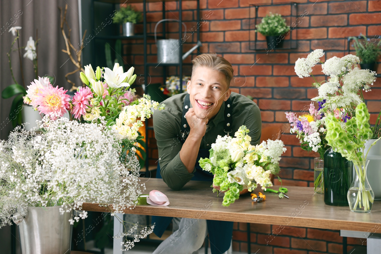 Photo of Professional florist with bouquet of flowers at wooden table in shop