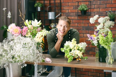 Photo of Professional florist with bouquet of flowers at wooden table in shop