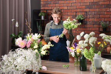 Photo of Professional florist with bouquet of flowers at wooden table in shop