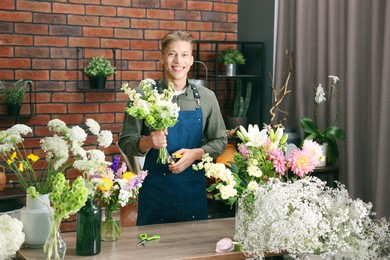 Photo of Professional florist with bouquet of flowers at wooden table in shop