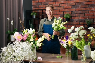 Photo of Professional florist with bouquet of flowers at wooden table in shop
