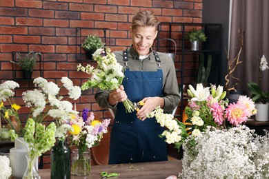 Photo of Professional florist with bouquet of flowers at wooden table in shop