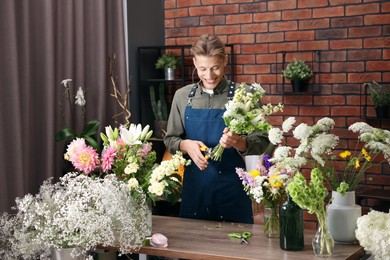 Photo of Professional florist with bouquet of flowers at wooden table in shop