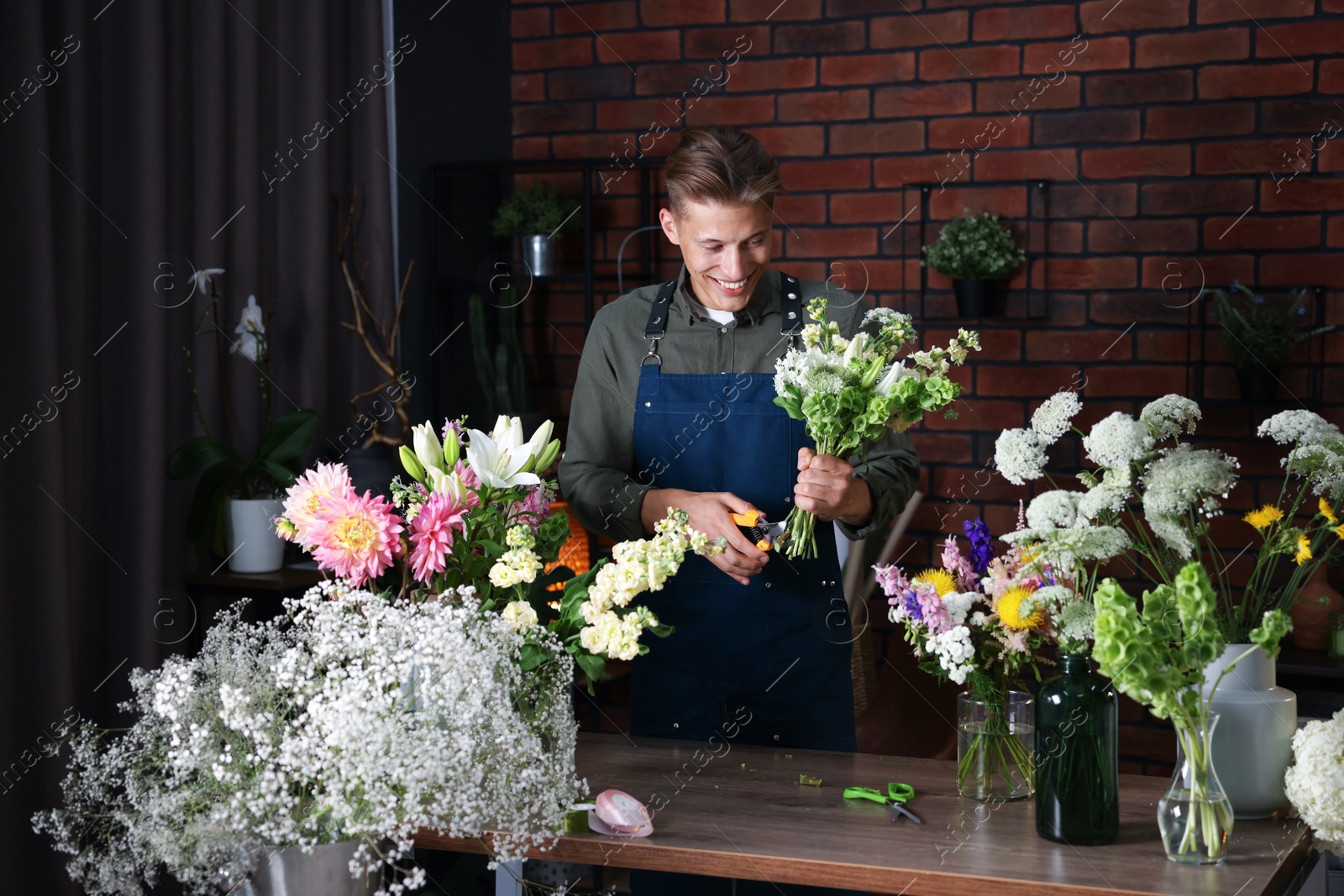 Photo of Professional florist with bouquet of flowers at wooden table in shop