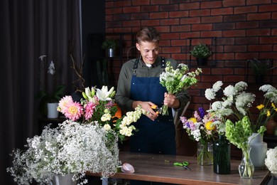 Photo of Professional florist with bouquet of flowers at wooden table in shop