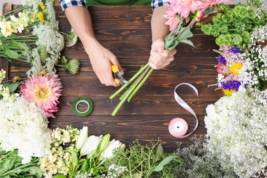 Photo of Professional florist making bouquet of flowers at wooden table, top view