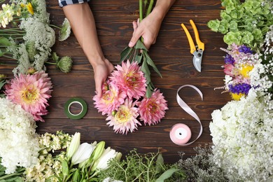 Photo of Professional florist making bouquet of flowers at wooden table, top view