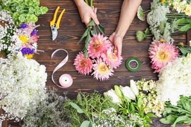 Photo of Professional florist making bouquet of flowers at wooden table, top view