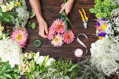 Photo of Professional florist making bouquet of flowers at wooden table, top view