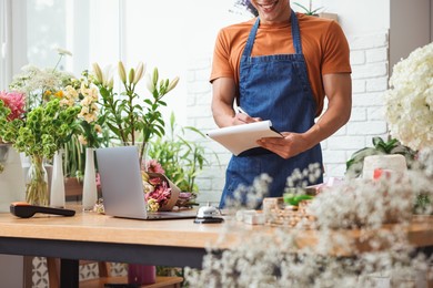 Photo of Professional florist working at wooden table in shop, closeup