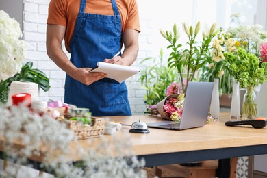 Photo of Professional florist working at wooden table in shop, closeup