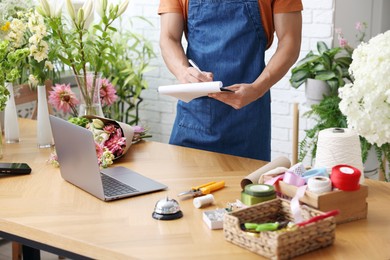 Photo of Professional florist working at wooden table in shop, closeup