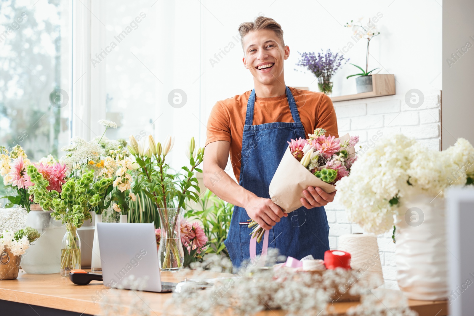 Photo of Professional florist with bouquet of flowers at wooden table in shop