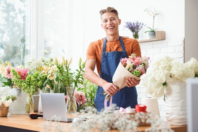 Photo of Professional florist with bouquet of flowers at wooden table in shop