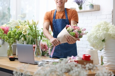 Photo of Professional florist with bouquet of flowers at wooden table in shop, closeup