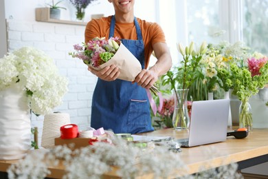 Photo of Professional florist with bouquet of flowers at wooden table in shop, closeup