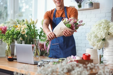 Photo of Professional florist with bouquet of flowers at wooden table in shop, closeup