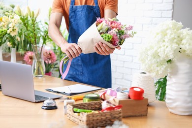 Photo of Professional florist with bouquet of flowers at wooden table in shop, closeup