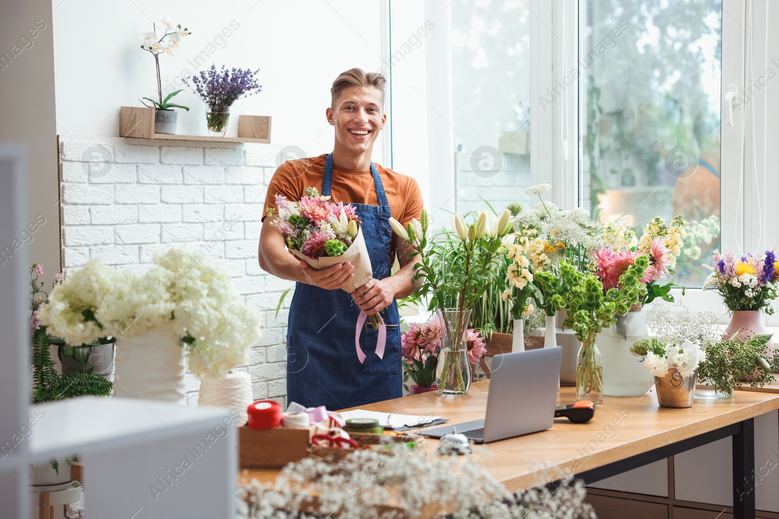 Photo of Professional florist with bouquet of flowers at wooden table in shop