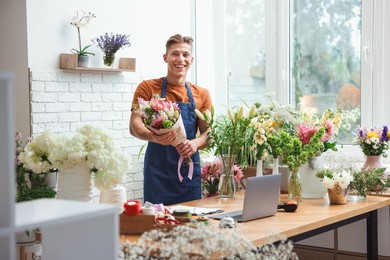 Photo of Professional florist with bouquet of flowers at wooden table in shop