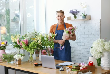 Photo of Professional florist with bouquet of flowers at wooden table in shop