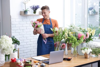 Photo of Professional florist with bouquet of flowers at wooden table in shop