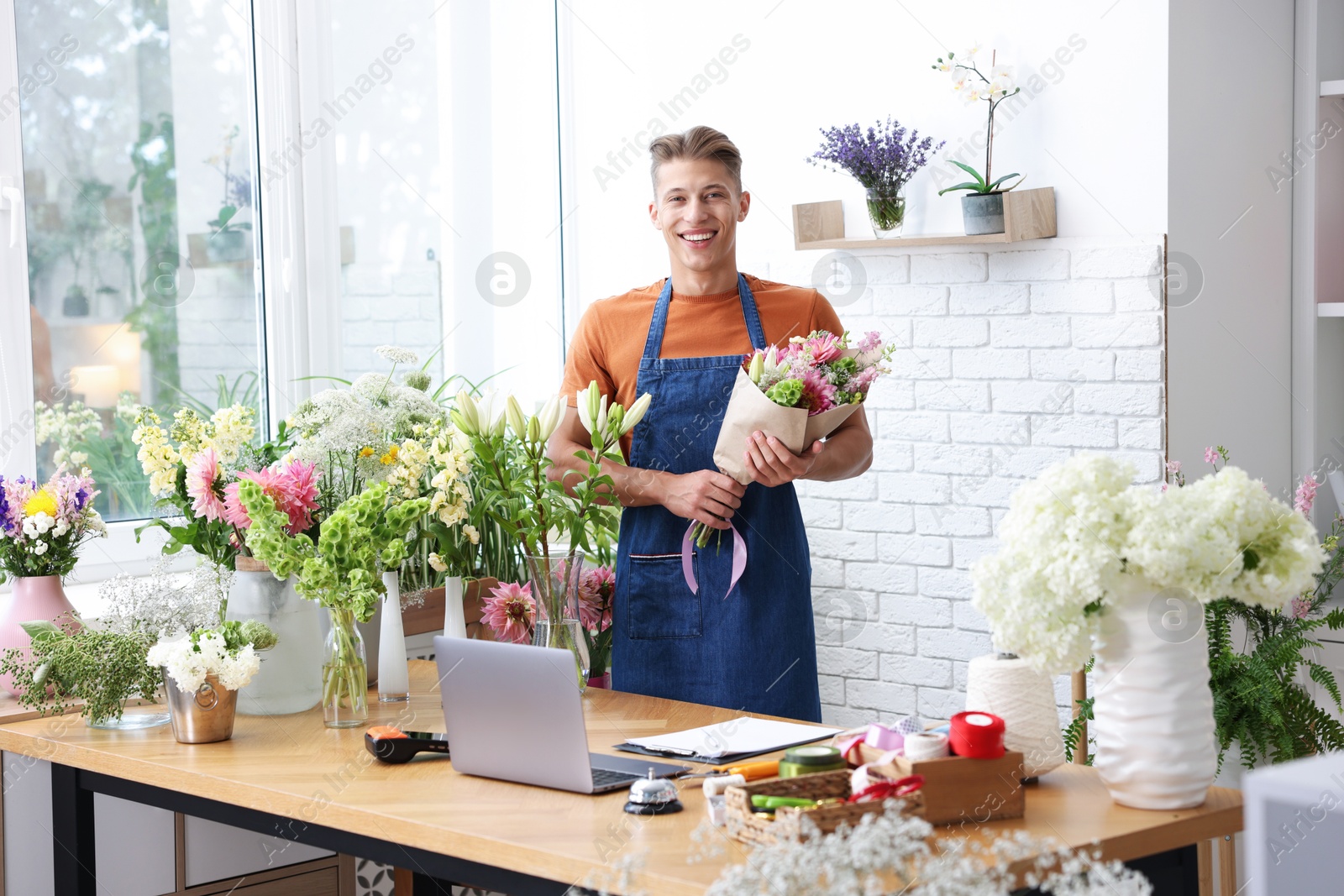 Photo of Professional florist with bouquet of flowers at wooden table in shop