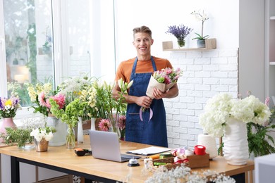 Photo of Professional florist with bouquet of flowers at wooden table in shop