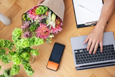 Photo of Professional florist with laptop working at wooden table, top view