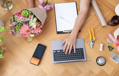 Photo of Professional florist with laptop working at wooden table, top view