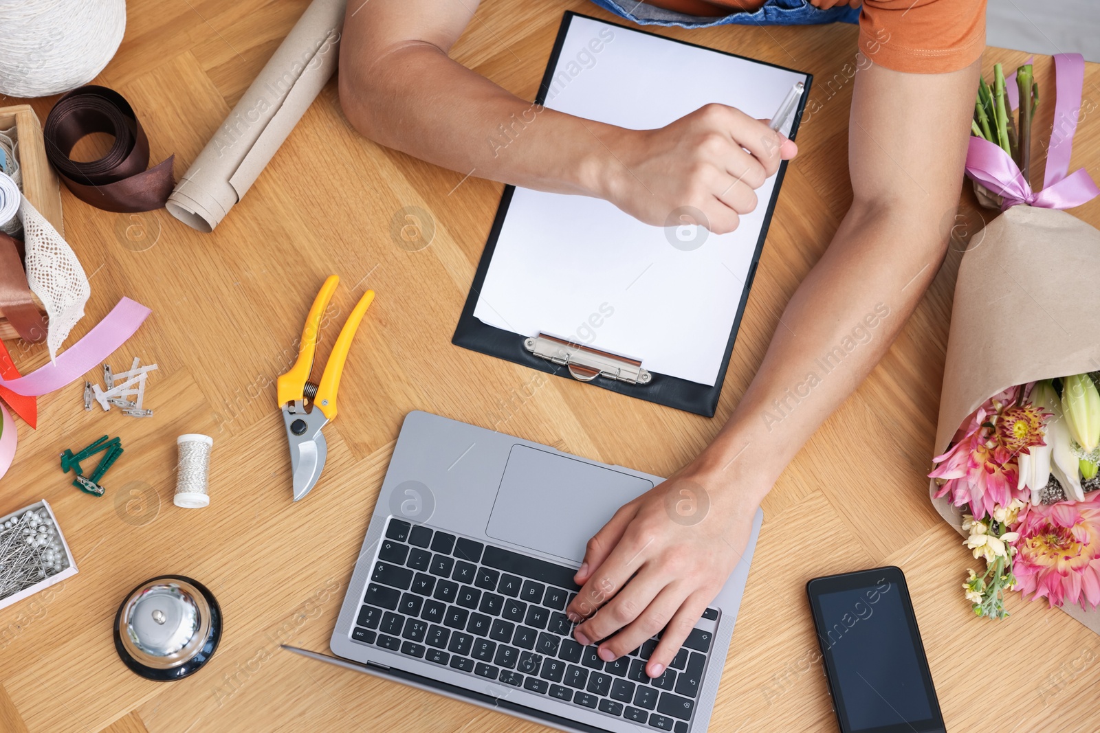 Photo of Professional florist with laptop working at wooden table, top view