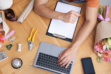 Photo of Professional florist with laptop working at wooden table, top view