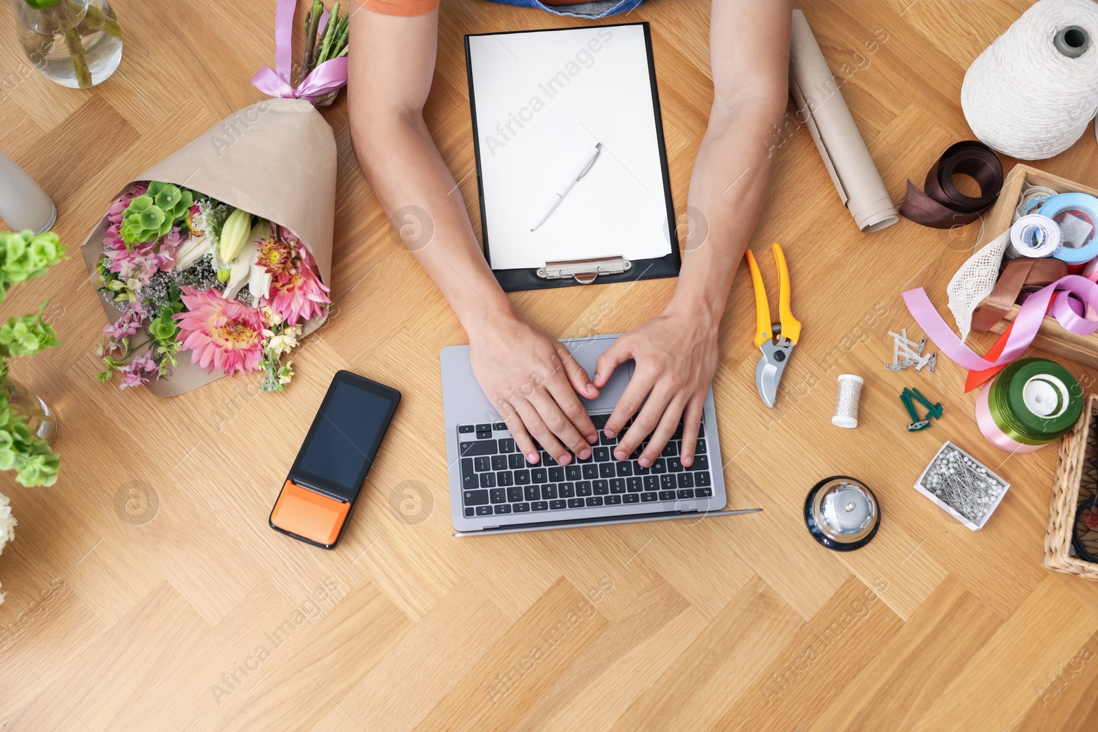 Photo of Professional florist with laptop working at wooden table, top view