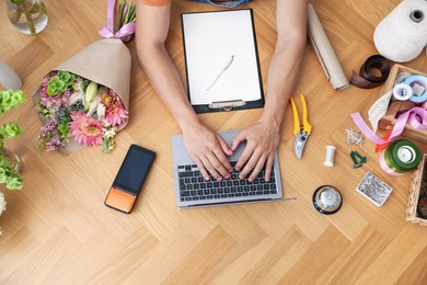 Photo of Professional florist with laptop working at wooden table, top view