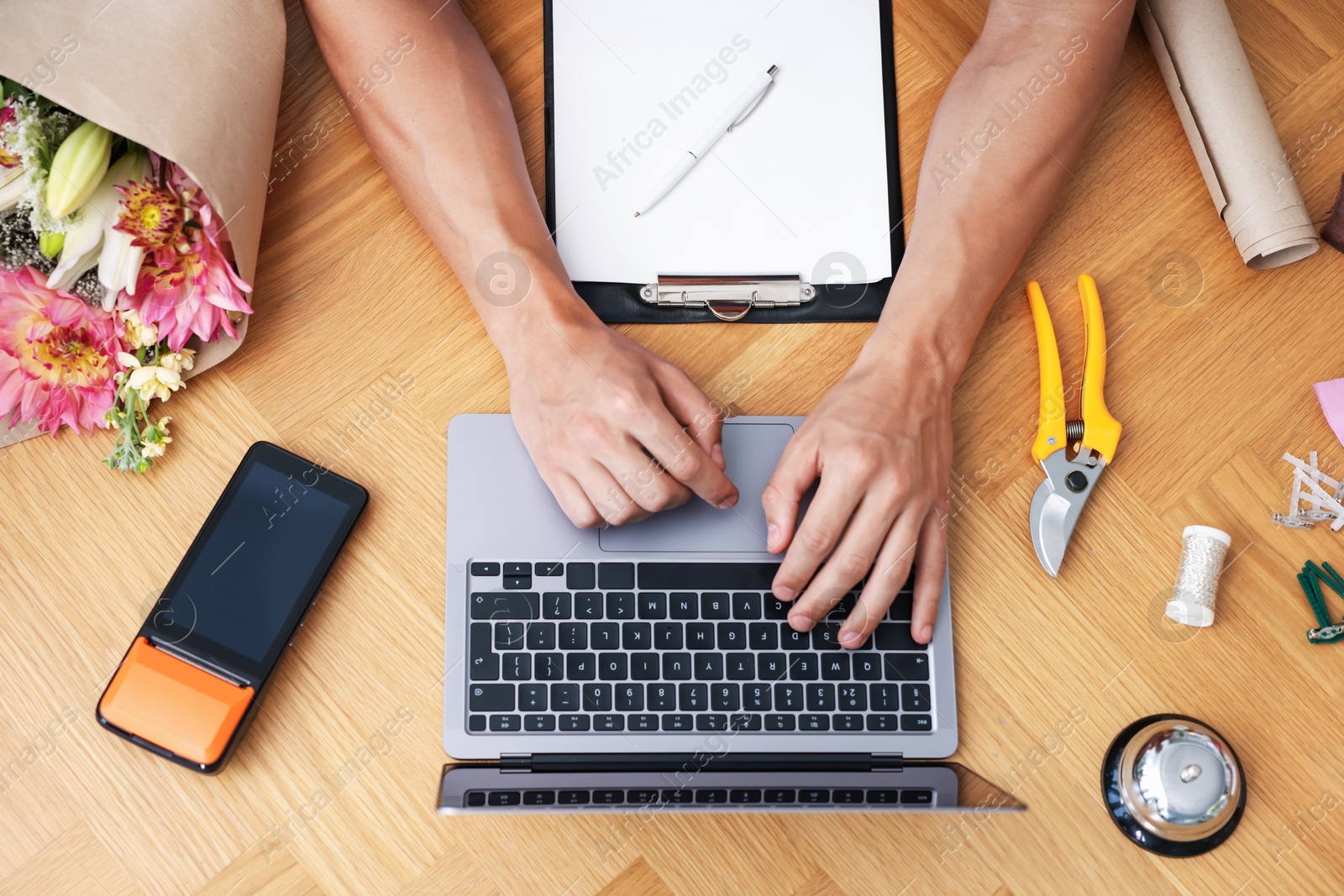 Photo of Professional florist with laptop working at wooden table, top view