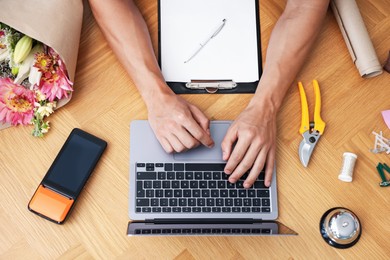 Photo of Professional florist with laptop working at wooden table, top view