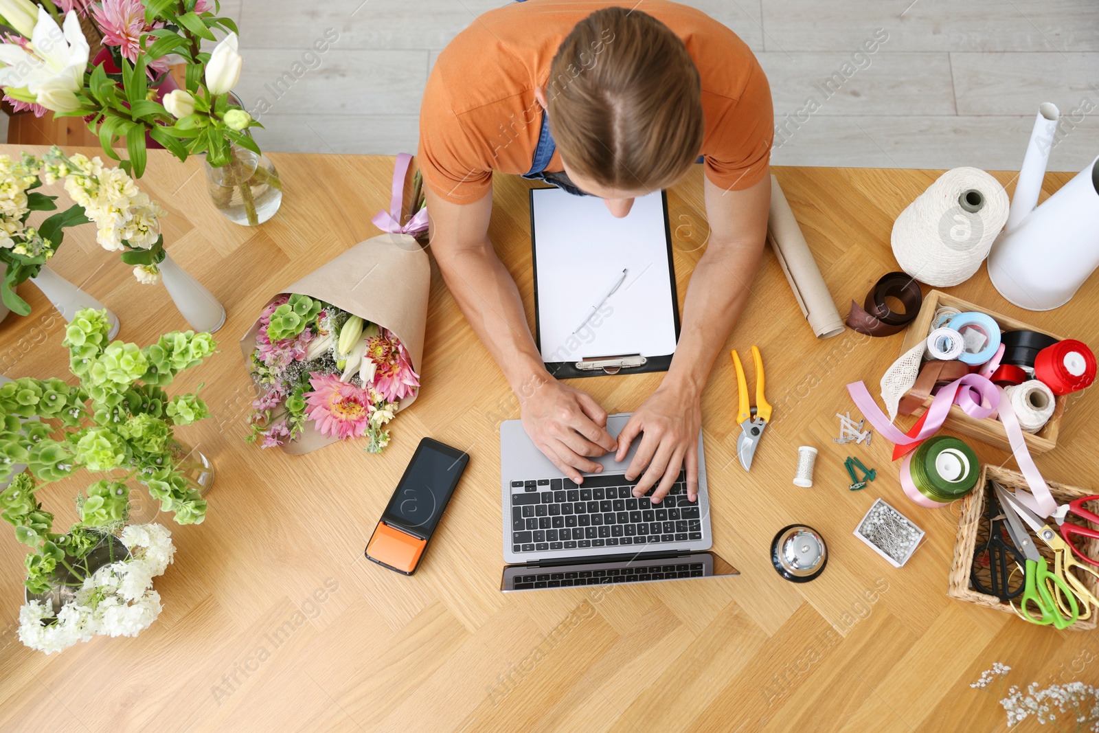 Photo of Professional florist with laptop working at wooden table, top view