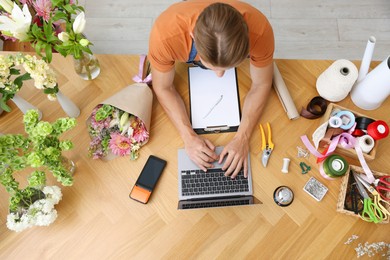 Photo of Professional florist with laptop working at wooden table, top view