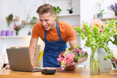 Photo of Professional florist with bouquet of flowers working at wooden table in shop