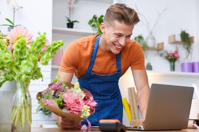 Photo of Professional florist with bouquet of flowers working at wooden table in shop