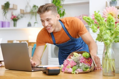 Photo of Professional florist with bouquet of flowers working at wooden table in shop