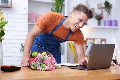 Photo of Professional florist with bouquet of flowers working at wooden table in shop