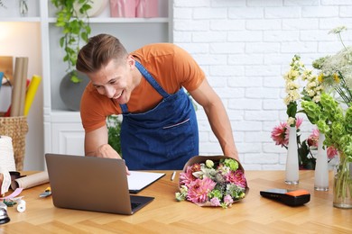 Photo of Professional florist with bouquet of flowers working at wooden table in shop