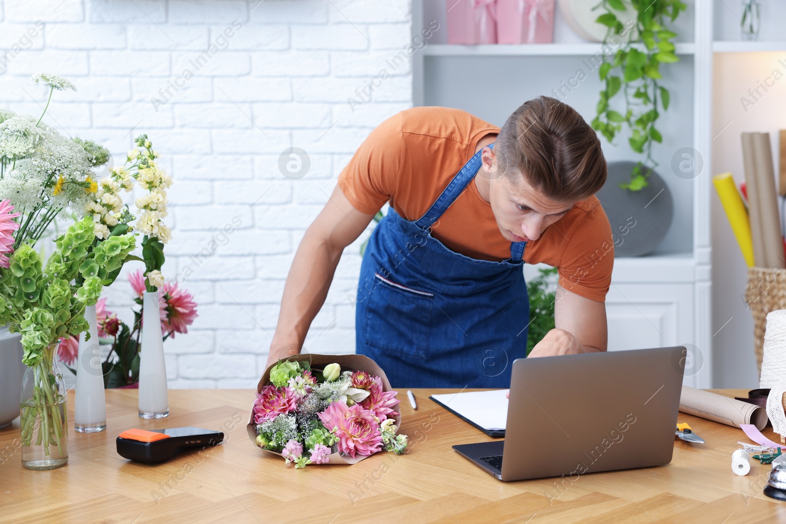 Photo of Professional florist with bouquet of flowers working at wooden table in shop
