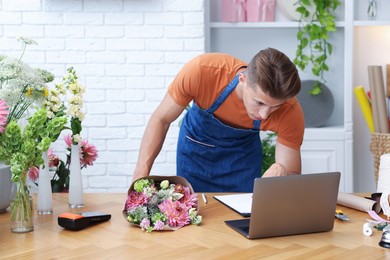 Photo of Professional florist with bouquet of flowers working at wooden table in shop